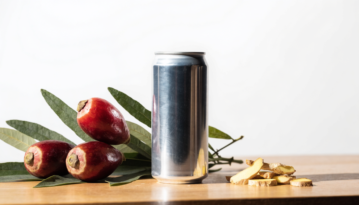 Canette de boisson énergisante bio entourée de guarana, de feuilles de maté et de gingembre sur une table en bois clair